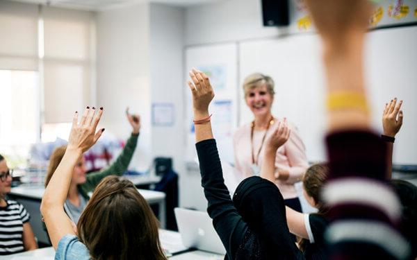 Students with their hands up responding to their teacher